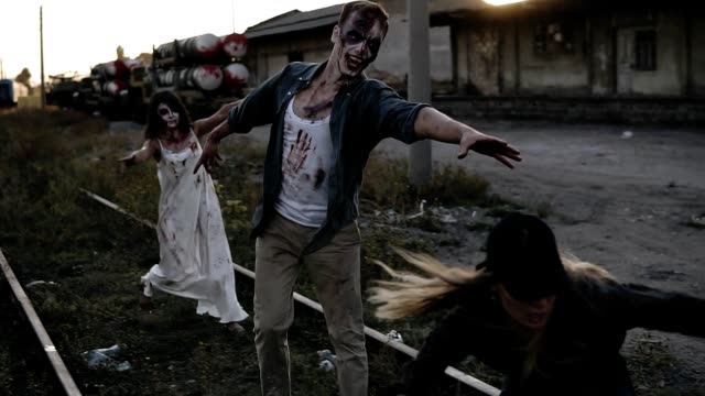 Young-woman-in-cap-running-away-from-a-creepy-zombie-pair,-Male-and-female-zombie-chasing-girl-going-by-railway.-The-girl-fell-and-zombie-caught-her.-Abandoned-town-on-the-background