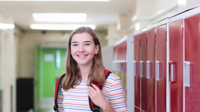 Portrait-Of-Female-High-School-Student-Walking-Down-Corridor-And-Smiling-At-Camera