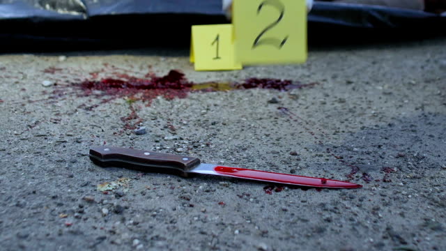 Group-of-forensic-experts-working-at-murder-site,-bloody-knife-lying-on-road