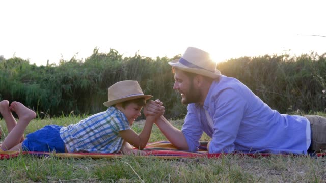 Vater-und-Sohn-spielen-zusammen-im-Armdrücken-und-Spaß-liegen-auf-Karomuster-in-ländlichen