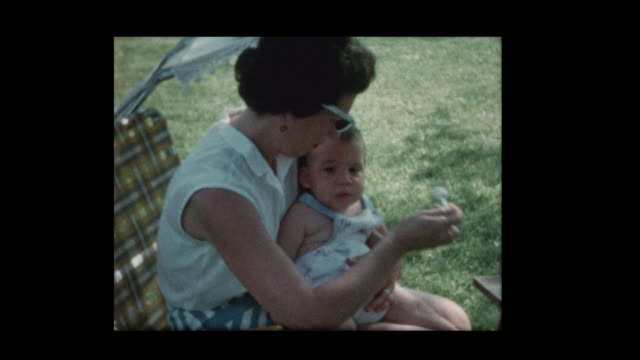 1960-Mom-Feeds-Baby-draußen-sitzen-auf-Liegestuhl
