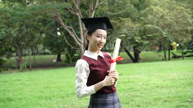 Diplomado-nueva-mujer-asiática-atractiva-joven-en-pose-uniforme-escolar-para-ver-las-fotos-en-el-parque-al-aire-libre---concepto-de-éxito-y-graduación