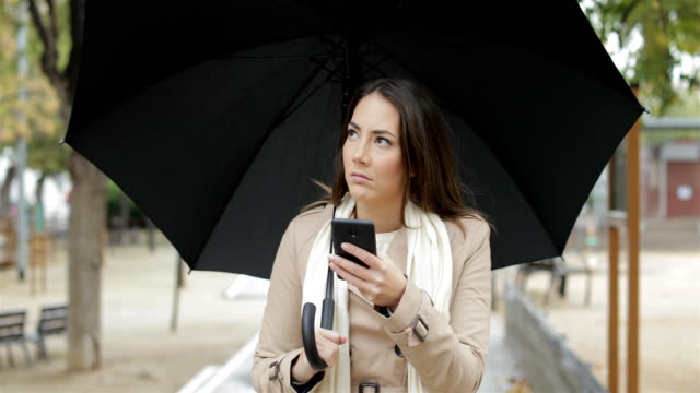 Mujer-frustrada-comprobación-de-aplicación-de-tiempo-bajo-la-lluvia