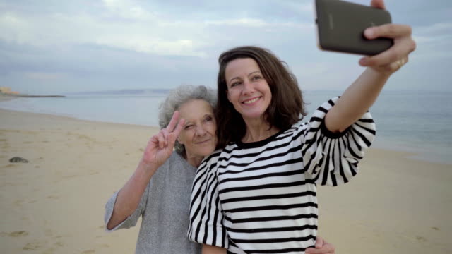 Adult-daughter-sticking-tongue-out-and-taking-selfie-with-mother