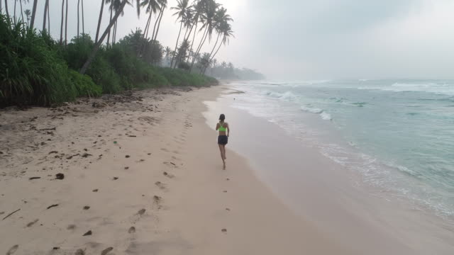Gesunde-Lebensweise-junge-Frau-läuft-am-tropischen-Strand-bei-Sonnenaufgang-am-Morgen