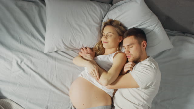 Happy-Young-Couple-Sleeping-Together-in-the-Bed,-Sweet-Loving-Young-People-Holding-Each-other-while-Sleeping.-Beautiful-Woman-is-Pregnant,-Loving-Partner-Supports-Her-By-Being-there-For-Her.