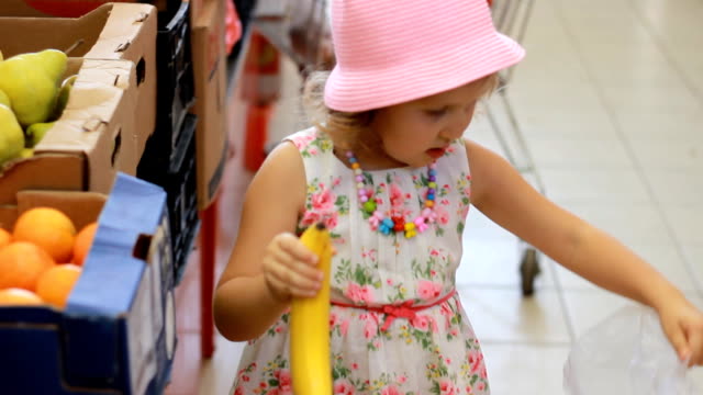 Child-girl-in-the-store-chooses-fruit-bananas.-Grocery-supermarket-and-shopping-trolley.