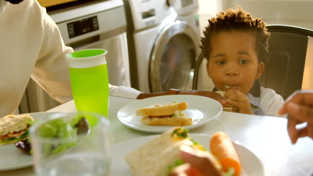 Vista-frontal-de-lindo-pequeño-hijo-negro-comiendo-comida-en-la-mesa-de-comedor-en-la-cocina-de-casa-cómoda-4k