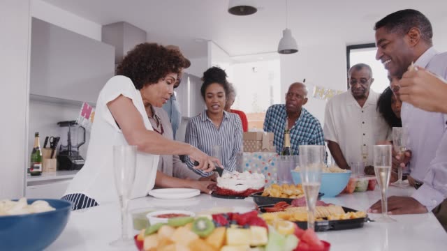 La-familia-negra-de-tres-generaciones-se-mantiene-alrededor-de-una-mesa-mientras-la-madre-corta-el-pastel-en-la-fiesta-de-cumpleaños