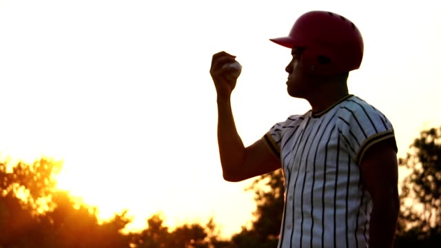 Jugador-de-béisbol-sosteniendo-una-pelota-de-béisbol-con-la-luz-del-atardecer