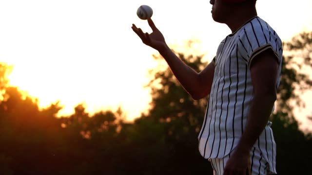 Jugador-de-béisbol-sosteniendo-una-pelota-de-béisbol-con-la-luz-del-atardecer