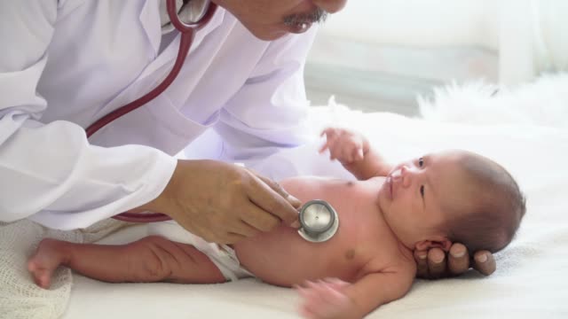 4K-Video-Selective-Focus-Medium-Schuss-von-männlichen-Arzt-untersucht-neugeborene-Mädchen-auf-weißem-Bett-und-weint-durch-Verwendung-Stethoskop-hören-Herzschlag
