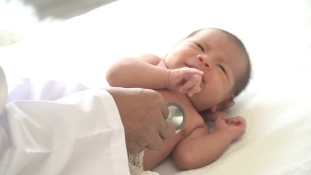 4K-Video-Selective-Fokus-hautnah-Schuss-von-männlichen-Arzt-untersucht-neugeborene-Mädchen,-die-sich-auf-weißes-Bett-legen-und-weinen-durch-Verwendung-Stethoskop-hören-Herzschlag