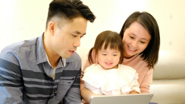 Asiatische-Eltern-Vater-und-Mutter-und-Tochter-spielen-mit-digitalen-Tablet-auf-dem-Sofa