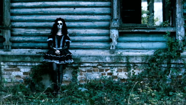 Die-Frau-mit-Halloween-Make-up-in-schwarzer-Kleidung-steht-vor-dem-Haus.-4K