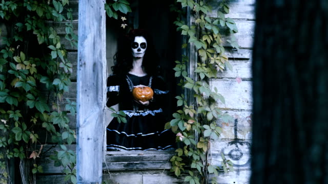 A-young-woman-with-halloween-make-up-holding-a-pumpkin-with-a-lighted-candle.-4K