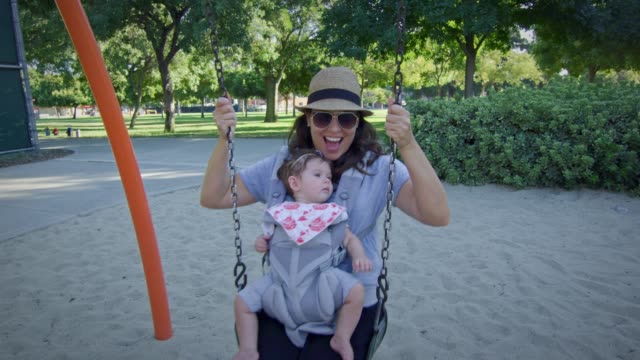 Woman-swinging-on-a-swing-with-baby-on-carrier-at-playground