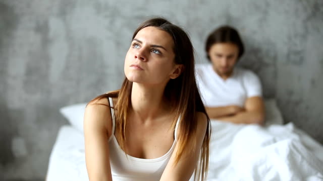 Unhappy-couple-sitting-apart-on-bed,-woman-worried-after-conflict