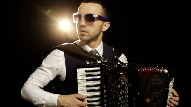 A-fashionable-musician-in-a-white-shirt-plays-the-accordion-in-the-studio-on-a-black-background.