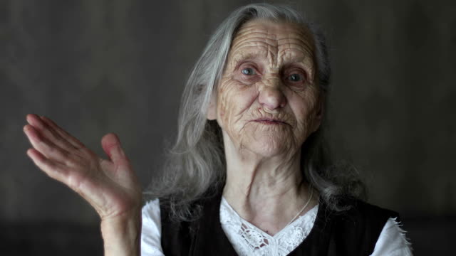 Portrait-of-old-woman-with-grey-hair-telling-story-and-gesticulating-hands.