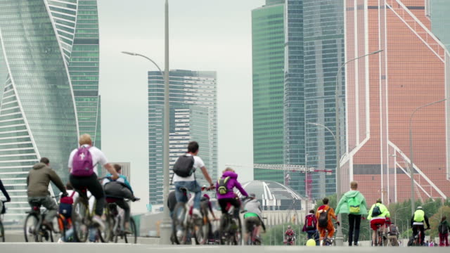 Bike-city-events-competition-in-background-of-skyscrapers,-crowd-of-cyclists-from-thousands-of-people-riding-bicycles,-unrecognizable-people-in-blur,-timelapse