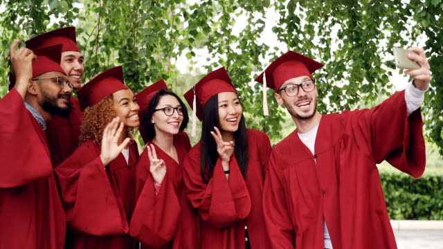 Slow-motion-of-cheerful-graduating-students-taking-selfie-with-smartphone,-young-people-are-posing,-showing-hand-gestures,-making-funny-faces-and-laughing.