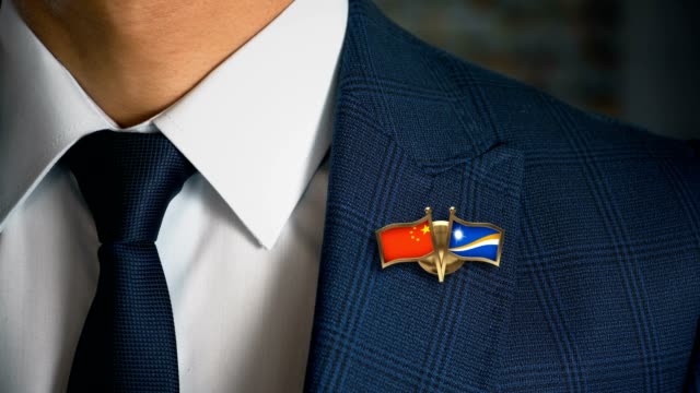 Businessman-Walking-Towards-Camera-With-Friend-Country-Flags-Pin-China---Marshall-Islands