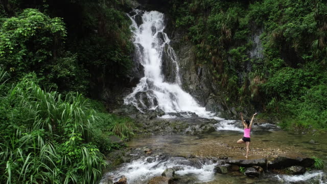 Gesunde-Lebensweise-Frau-Yoga-üben-in-der-Nähe-von-Wasserfall-im-Wald