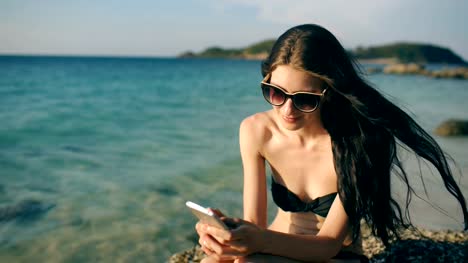 Hermosa-mujer-SMS-mensajes-de-texto-utilizando-la-aplicación-en-el-teléfono-inteligente-en-la-puesta-de-sol-playa-durante-las-vacaciones