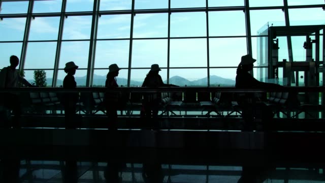 Silhouette-of-passengers-walking-with-luggage-in-a-busy-airport-terminal