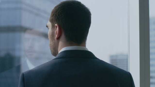Close-up-Shot-of-the-Thoughtful-Businessman-in-a-Suit-Standing-in-His-Office-and-Contemplating-Next-Big-Business-Deal,-Looking-out-of-the-Window.-Big-City-Business-District-Panoramic-Window-View.