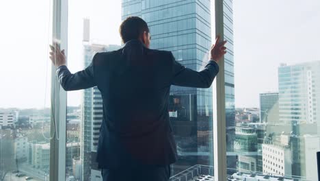 Following-Shot-of-the-Confident-Businessman-in-a-Suit-Walking-Through-His-Office-and-Looking-out-of-the-Window-Thoughtfully.-Stylish-Modern-Business-Office-with-Personal-Computer-and-Big-City-View.