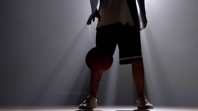 Ein-Basketball-Spieler-dribbeln-Ball-im-nebligen-dunklen-Raum-mit-Flutlicht