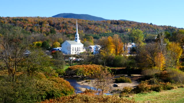 wide-shot-of-a-church-in-stowe-with-a-hill-covered-in-fall-foliage