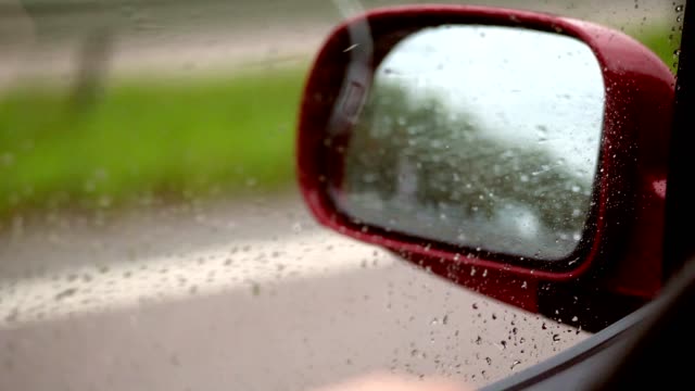 close-up,-Wassertropfen-auf-Seitenfenster-des-Autos-während-der-Fahrt.-Vom-starken-Wind-fließen-Tröpfchen-das-Glas-nicht-ab,-sondern-nach-oben.-durch-Fenster-sehen-Sie-Seite-Rückspiegel