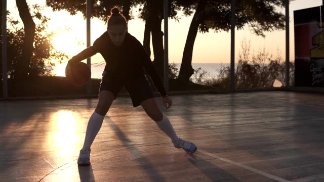 Junge-kaukasischen-weiblichen-Basketball-Spieler-dribbeln-und-üben-Kugel-Handhabung-Fähigkeiten-auf-Platz.-Morgen-Dämmerung,-scheint-die-Sonne-auf-dem-Hintergrund