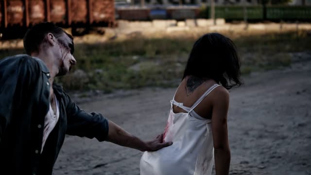 Halloween-horror-filming-concept.-Picture-of-creepy-male-and-female-ghost-or-zombie-walking-outdoors.-Man-trying-to-touch-the-girl-from-the-back.-Industrial,-abandoned-town-on-the-background
