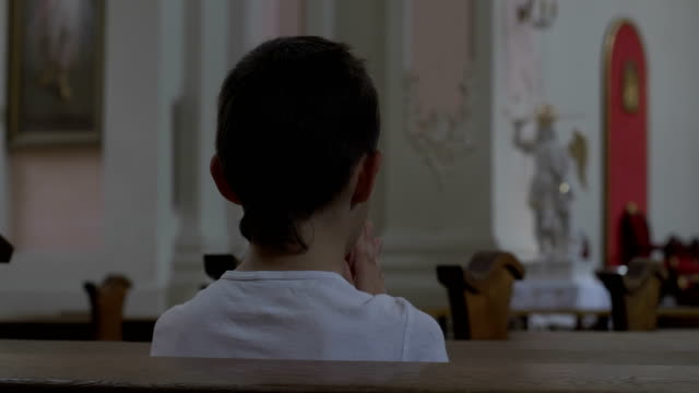 serious-boy-praying-in-the-Church-alone,-back-view