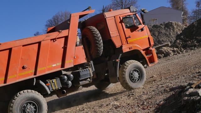 Camión-de-volquete-naranja-en-territorio-industrial-en-fondo-de-colinas-de-arena