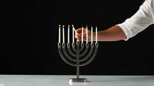 Hand-lighting-the-remaining-white-candles-in-a-Jewish-menorah-from-a-single-candle,-close-up,-front-view