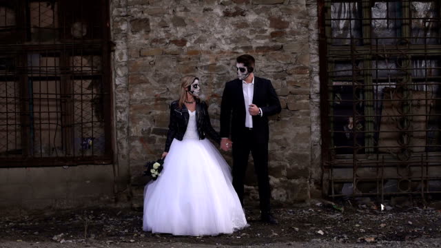 Paar-in-Brautkleider-mit-Halloween-Make-up-in-der-Nähe-einer-alte-Mauer.