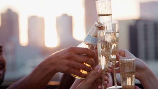Close-Up-Of-Friends-With-Drinks-Making-A-Toast-On-Rooftop-Terrace-With-City-Skyline-In-Background