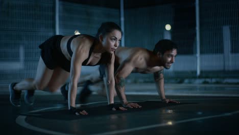 Lächeln-gerne-sportliche-Fitness-paar-tun-Mountain-Climber-Übungen.-Training-erfolgt-in-einem-eingezäunten-Basketballfeld-im-Freien.-Nacht-Aufnahmen-nach-Regen-in-einer-Wohngegend.