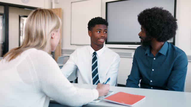 Father-And-Teenage-Son-Having-Discussion-With-Female-Teacher-At-High-School-Parents-Evening