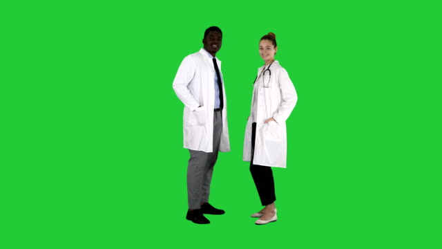 Two-caucasian-and-afro-american-smiling-doctors-standing-looking-in-to-camera-on-a-Green-Screen,-Chroma-Key