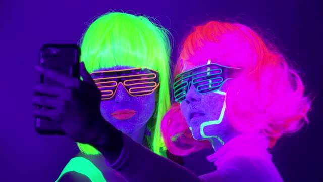 Langsame-Motin-von-schönen-sexy-Frauen-mit-fluoreszierenden-Make-up-und-Kleidung-Selfie-Aufnahme-im-Neonlicht.-Night-Club,-Party-Konzept.