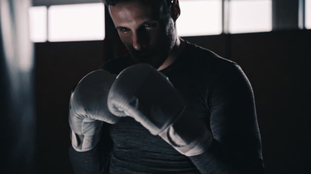 Ajuste-el-boxeador-entrenando-en-un-saco-de-boxeo-en-un-estudio-de-boxeo-interior