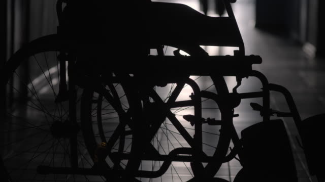 Silhouette-der-Frau-hinkend-an-Rollstuhl-entlang-Krankenhaus-Flur