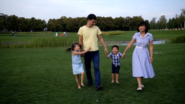 Freudige-asiatischen-Familie-zu-Fuß-halten-Hände-im-park
