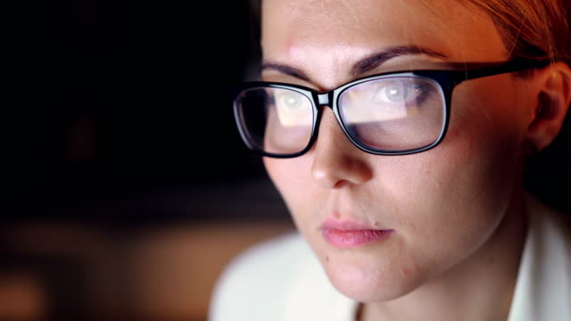 Close-up-shot-of-beautiful-young-woman-wearing-glasses-using-computer-working-late-at-night-in-dark-office-room.-Businesspeople,-work-and-youth-concept.